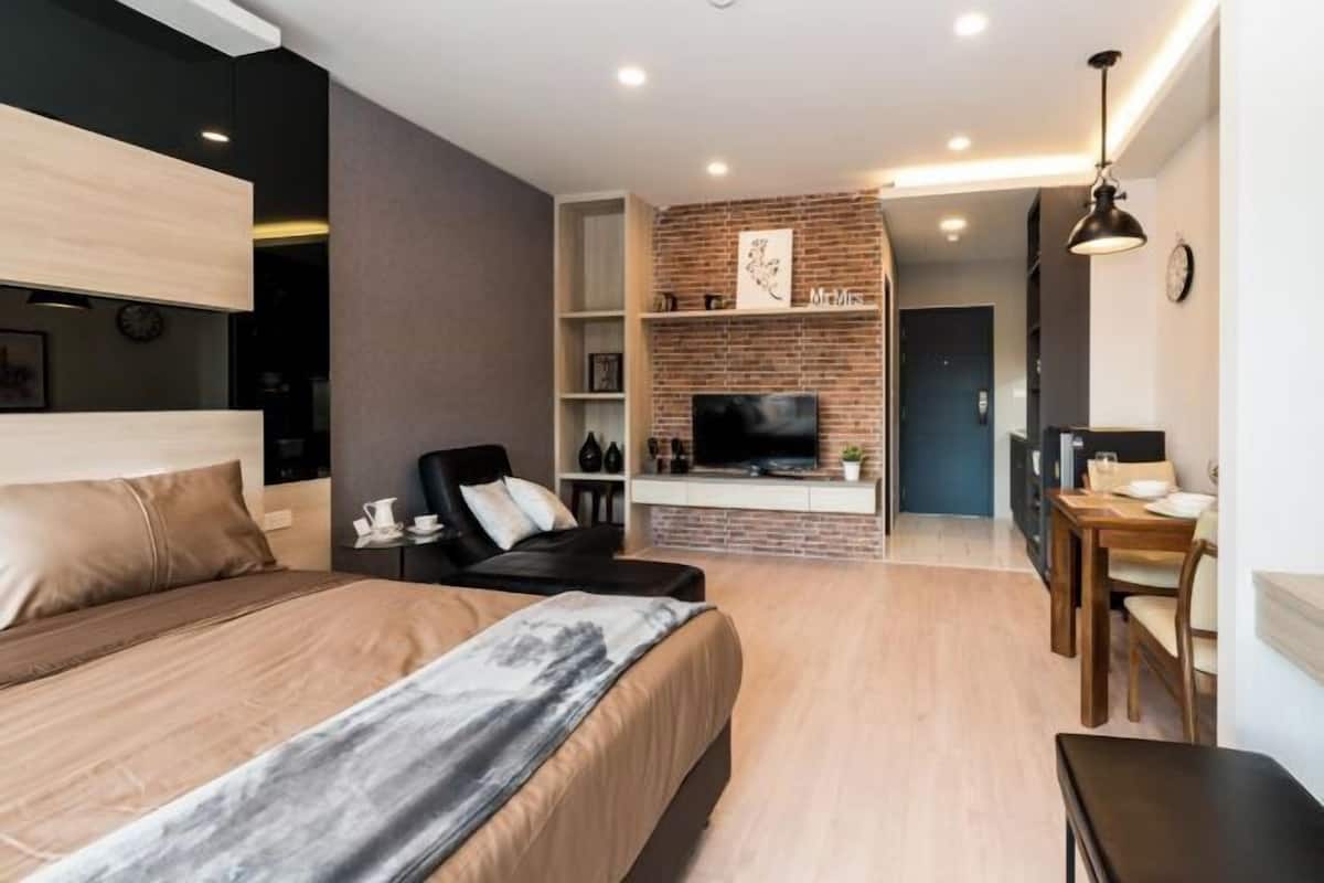Une chambre moderne avec un lit, un bureau, une chaise, un téléviseur et un mur en briques.