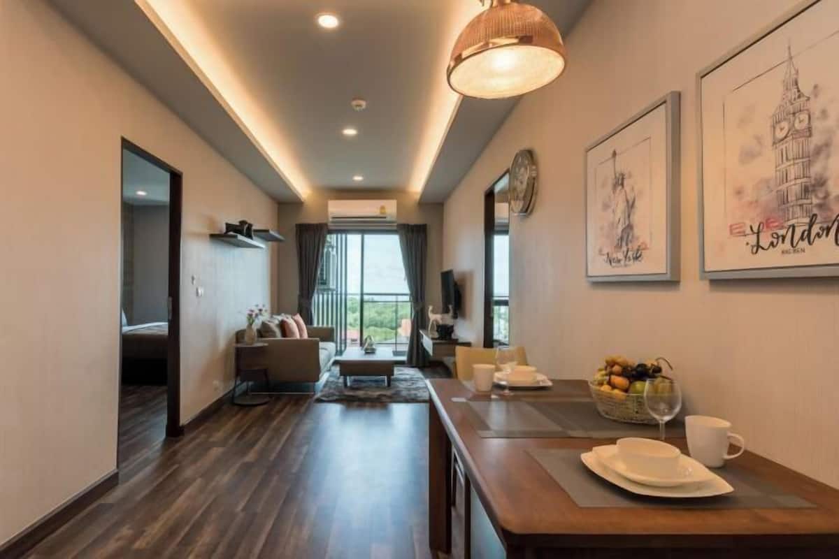 Une chambre d’hôtel moderne avec un plancher en bois, un coin repas avec une table dressée pour deux personnes, un canapé et une grande fenêtre donnant sur un paysage agréable.