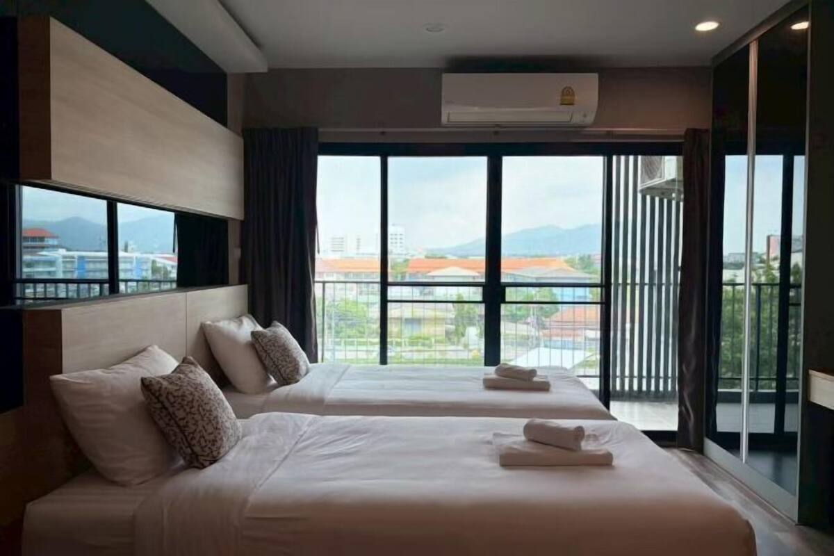 Une chambre d’hôtel avec deux lits, une grande fenêtre donnant sur un beau paysage, un système de climatisation et un balcon.