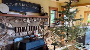 A rustic interior with a stone fireplace, a small Christmas tree, and a sign reading "ROUGH & READY LIVING EST. 2025". - Rough & Ready Ranch Retreat- 4 bed/3 bath home w/ gorgeous views (Rough and Ready)