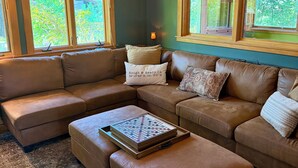 A living room with a sectional sofa, a coffee table, and a chandelier. There are windows with green foliage visible outside. - Rough & Ready Ranch Retreat- 4 bed/3 bath home w/ gorgeous views (Rough and Ready)