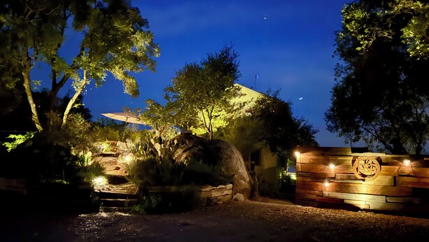A nighttime view of a landscaped area with a pathway leading to a building with a wooden fence and illuminated signage. - Rough & Ready Ranch Retreat- 4 bed/3 bath home w/ gorgeous views (Rough and Ready)