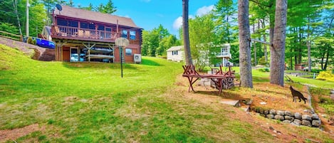 A cabin with a deck, surrounded by trees and a grassy area.