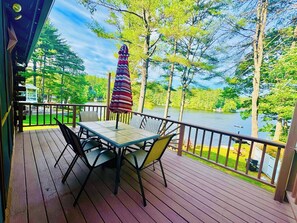 Eine Holzterrasse mit Tisch und Stühlen, mit Blick auf einen See, Bäume und einen Steg.
