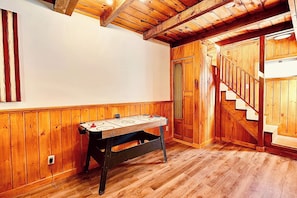 Een kamer met houten lambrisering, een tafelvoetbaltafel en een trap.