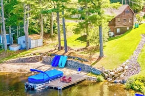 A lakeside property with a dock, a boat, and a small waterfall. - Cozy Lakefront Log Cabin•Year Round Family Retreat (Wakefield)