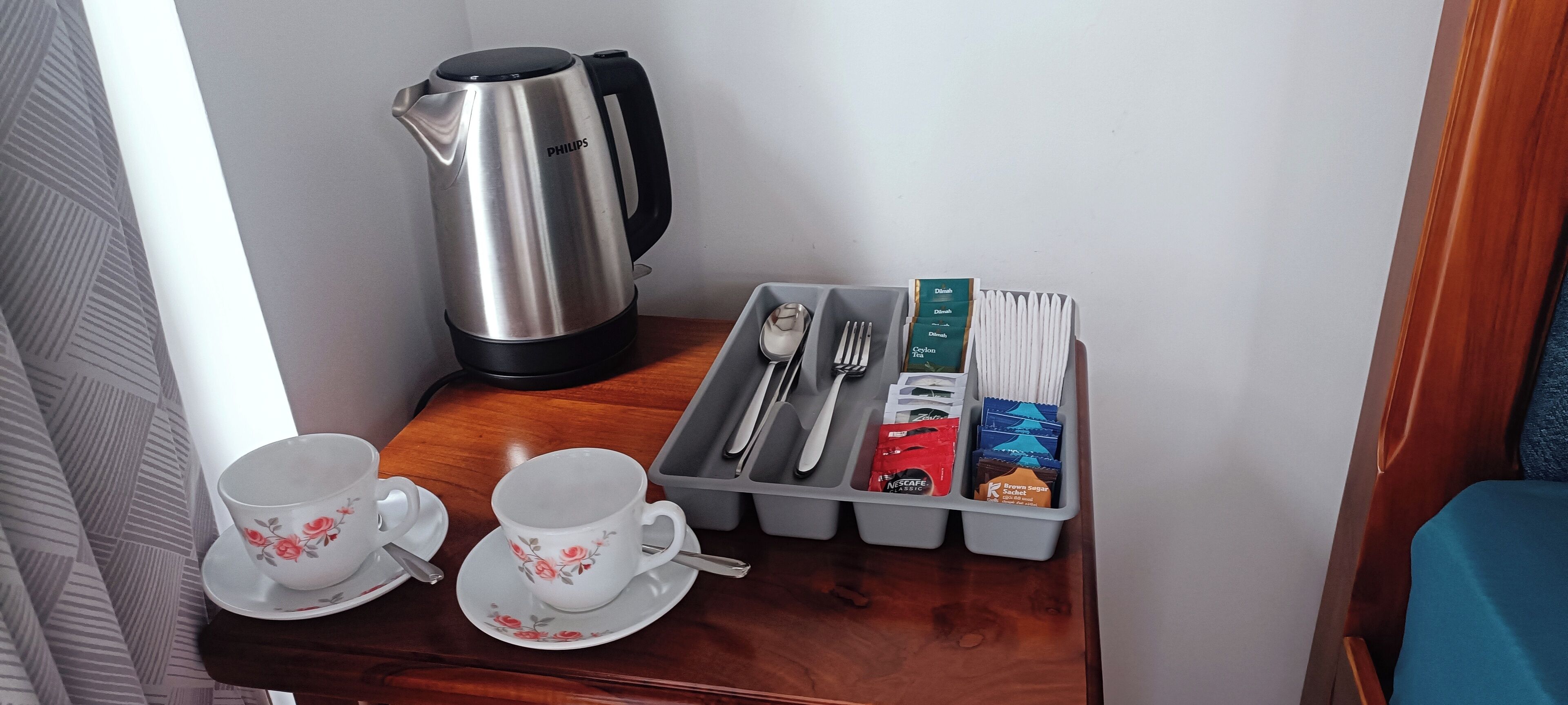 A neatly arranged breakfast setup with a kettle, two cups, a tray with utensils, and packaged food items.