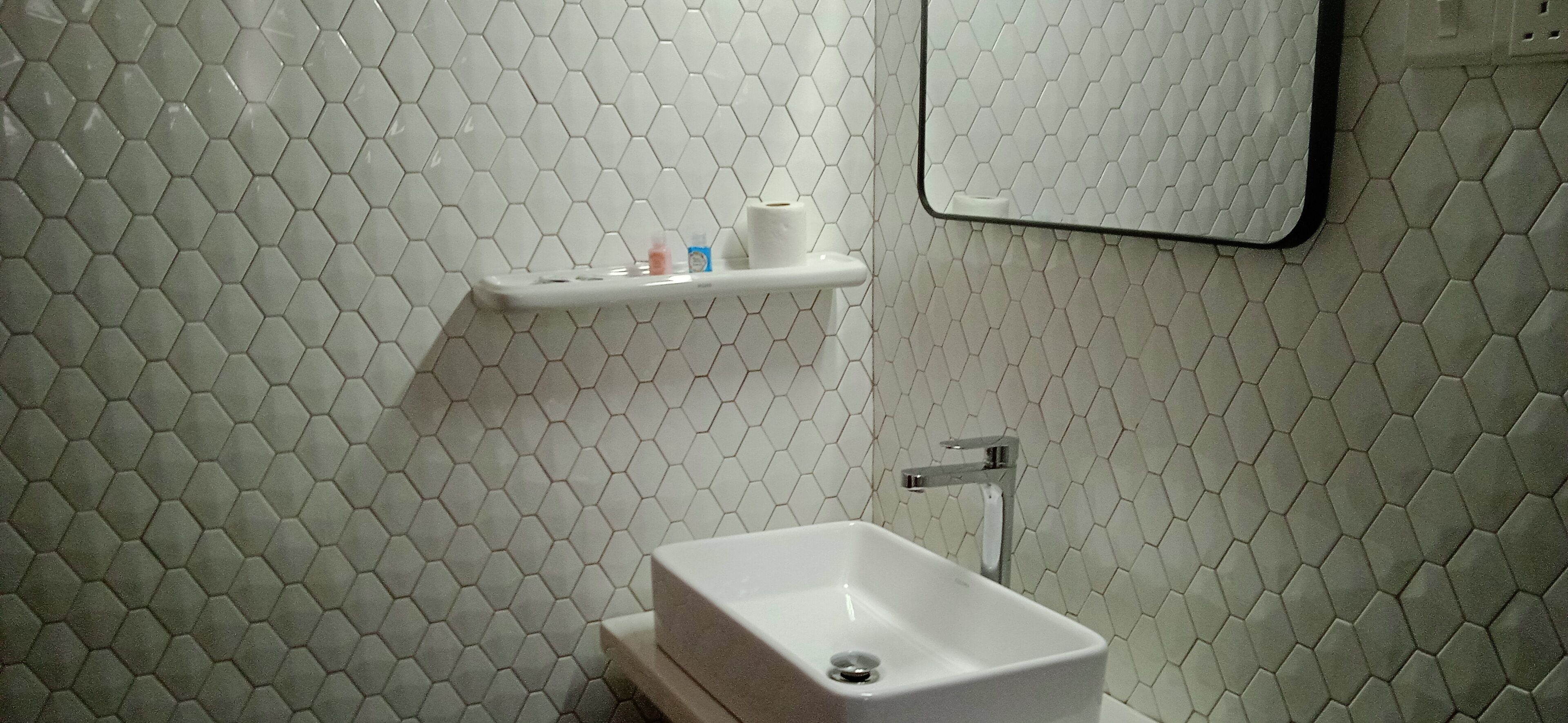 A bathroom with a white hexagonal tile backsplash, a white sink, and a mirror above the mirror.