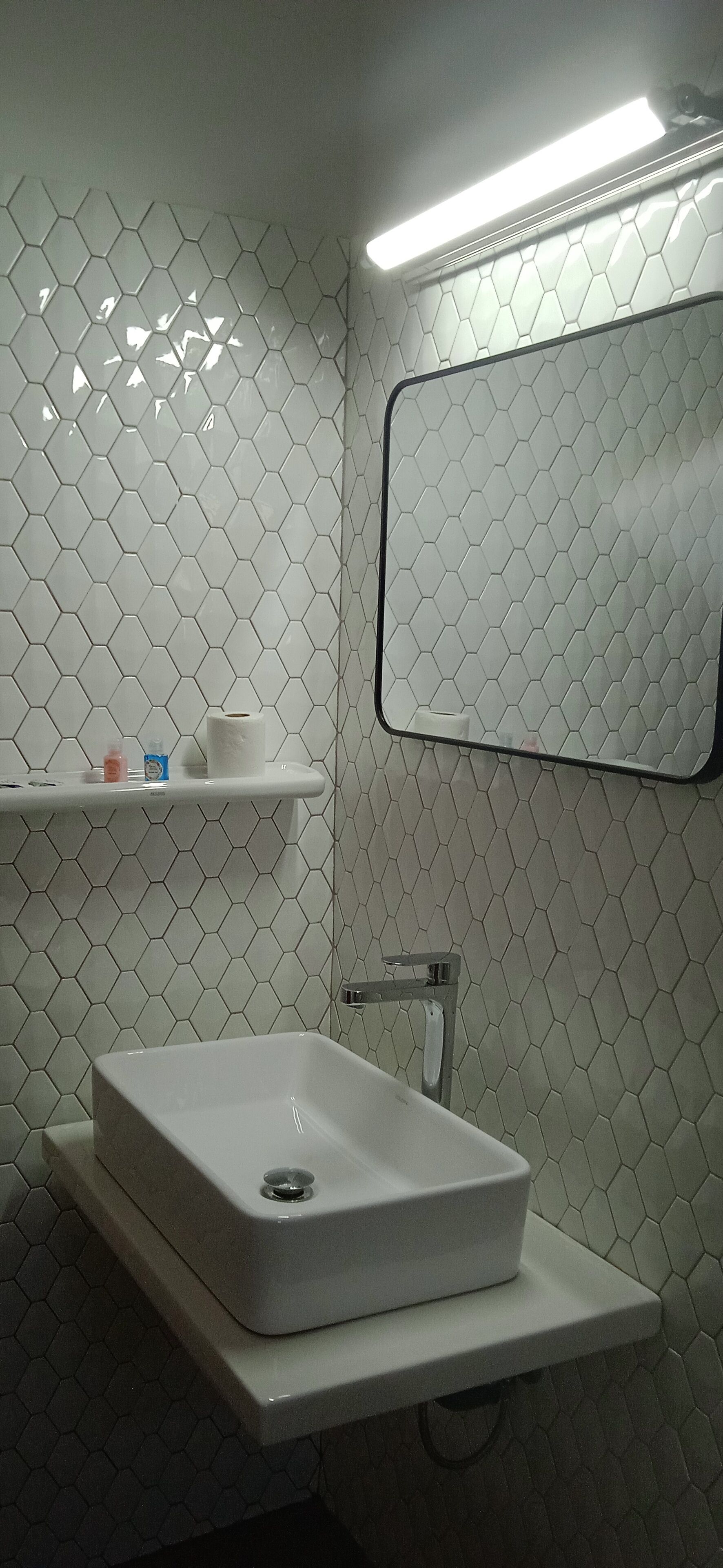 A bathroom with a white sink, a mirror, and a shelf with toiletries.