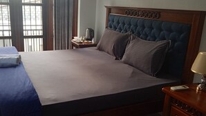 A hotel room with a large bed, a wooden headboard, a nightstand with a lamp, and a view through a window with bars. - Sweet Home Ja-Ela (Ja-Ela)