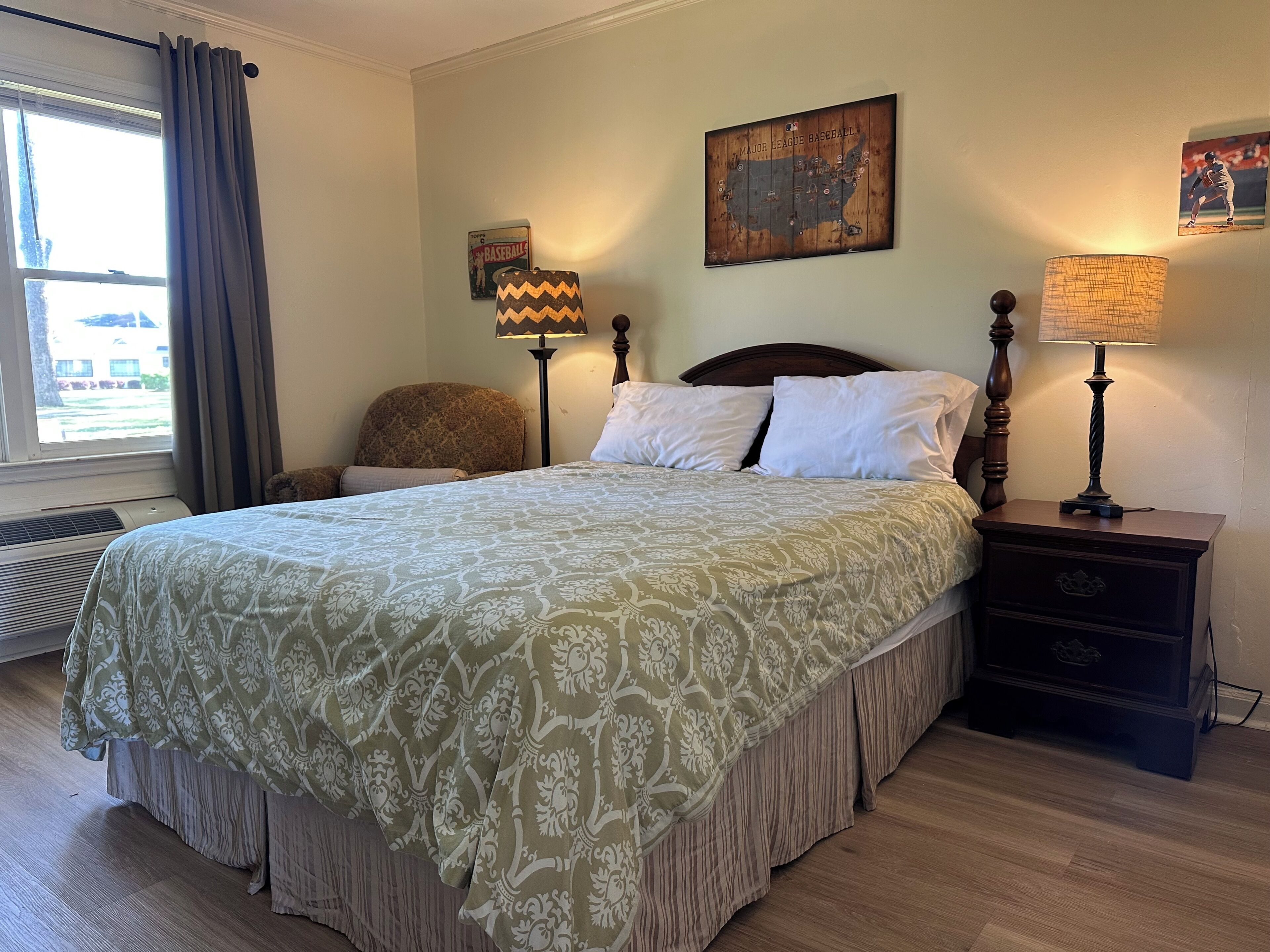 Een netjes ingerichte slaapkamer met een groot bed, twee nachtkastjes met lampen, een stoel en een wereldkaart aan de muur.