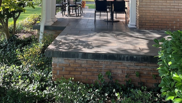 A covered patio with white columns, outdoor tables and chairs, and a brick wall.