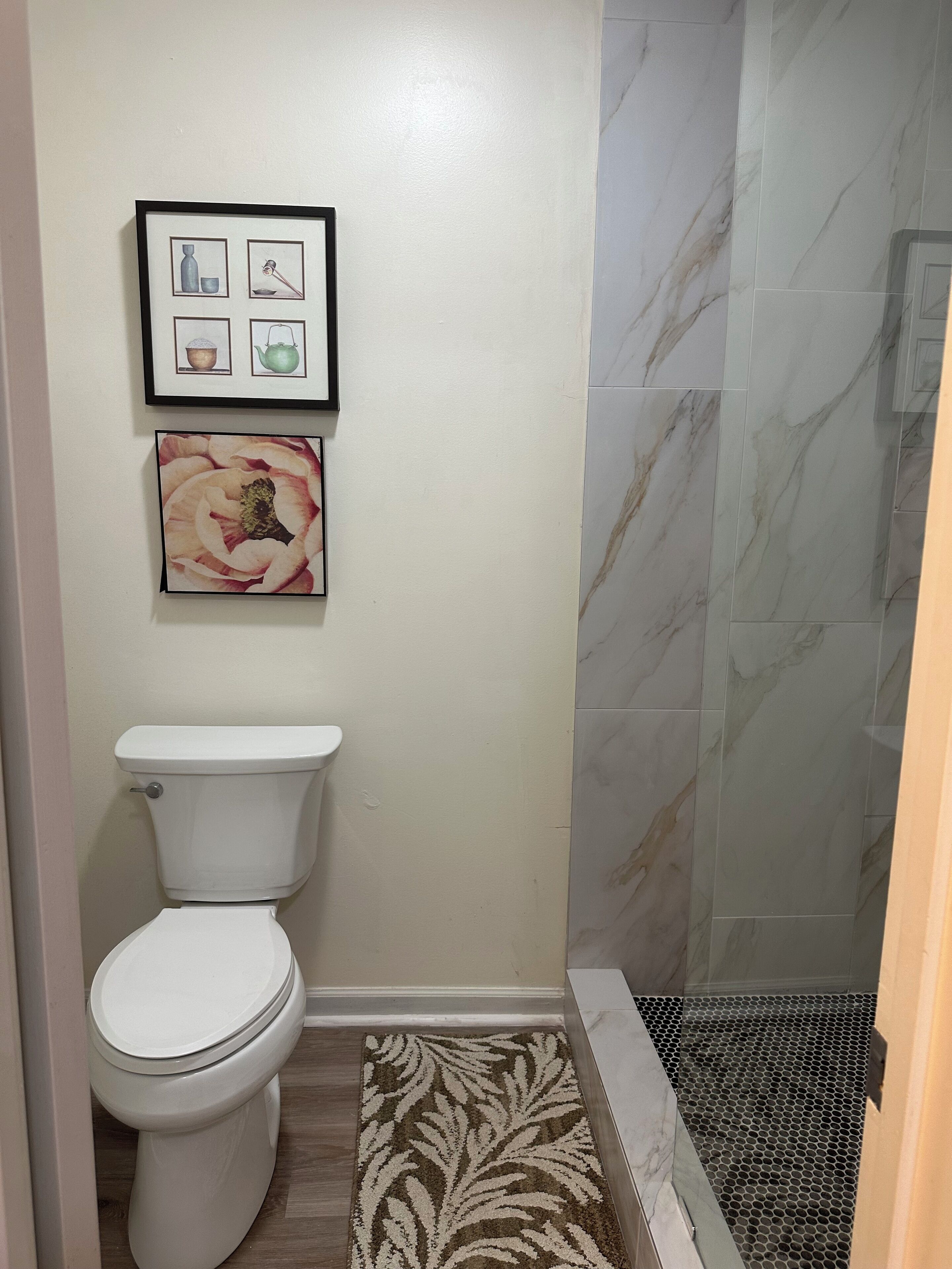 Casa de banho com sanita, um quadro com uma flor e zona de duche com parede de mármore.