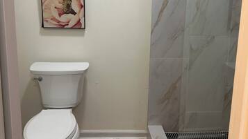 Casa de banho com sanita, um quadro com uma flor e zona de duche com parede de mármore.