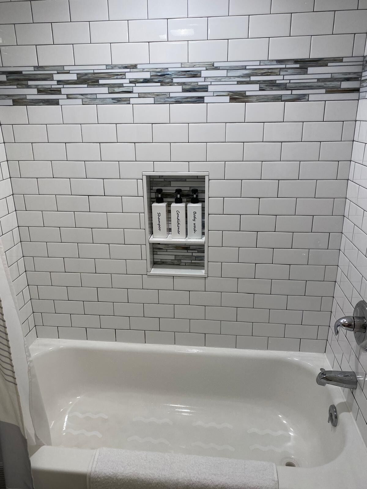 A bathroom with a white bathtub, a shower, and a shelf with toiletries.