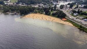 An aerial view of a beach with a sandy shore, a road adjacent to the beach, and a body of water. - Cozy 2-Bed Lakefront Weirs Beach (Laconia)