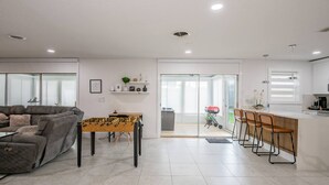 A modern living room with a sofa, a foosball table, and a dining area with a kitchen in the background. - Riverside Retreat w Fireplace (Daytona Beach)