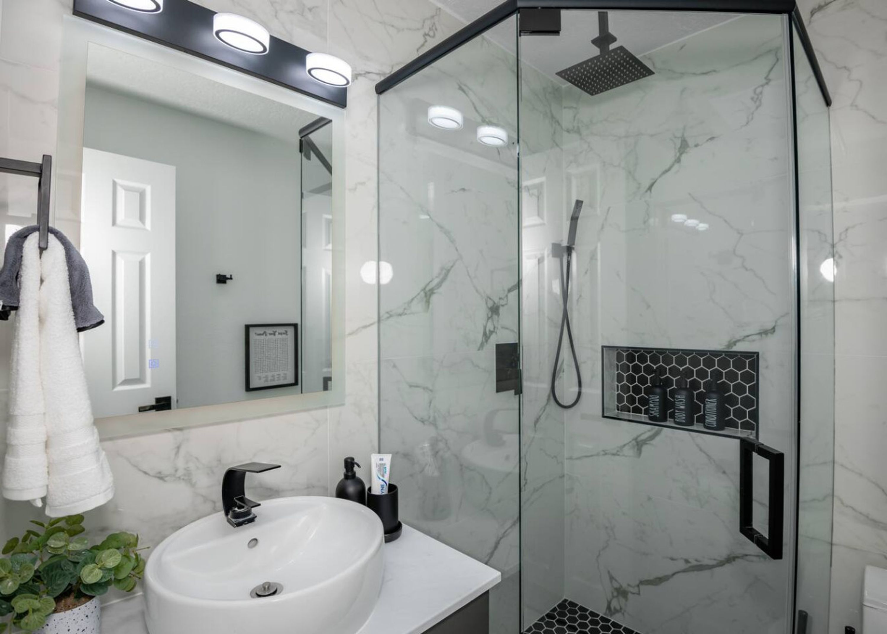A modern bathroom with a glass-enclosed shower, a white sink, and a mirror above it.