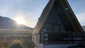 Un bâtiment triangulaire avec un toit en pente, entouré d’un champ verdoyant et avec une montagne en arrière-plan.