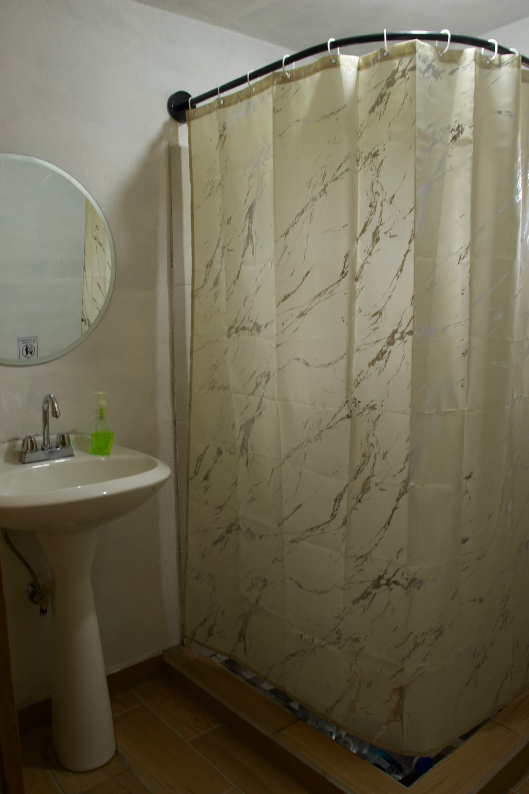 Un baño con cortina de ducha con estampado de mármol, un lavamanos blanco y un espejo.