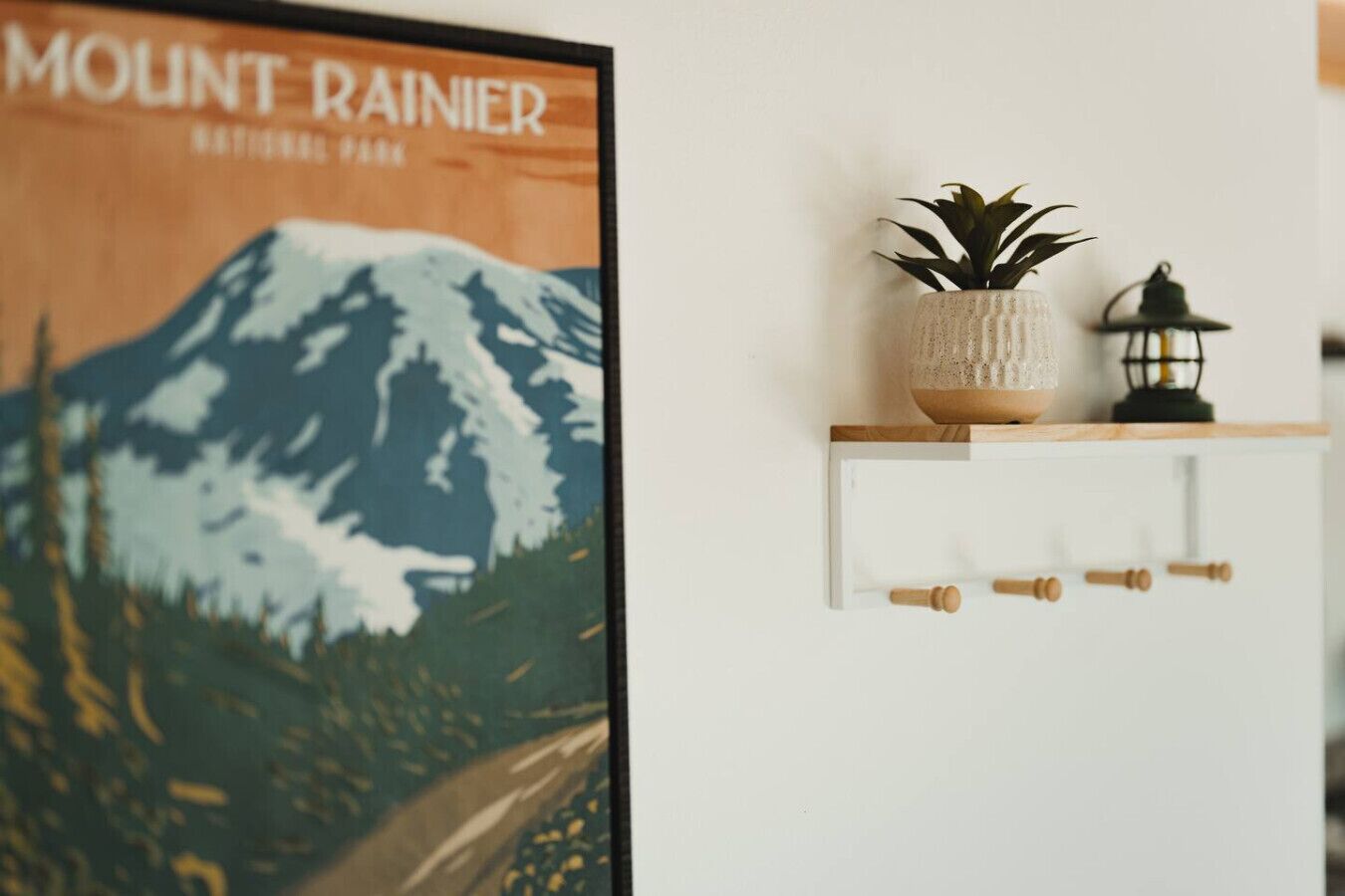 Póster del Parque Nacional del Monte Rainier, un armario blanco con una planta y un farol, e interruptor de luz en la pared.