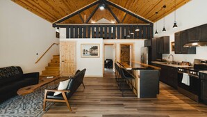 Un amplio salón con techo de madera, una cocina con armarios oscuros y un comedor con barra.
