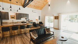 Amplia sala de estar con un sofá de cuero negro, una mesa de centro de madera y una cocina con barra.