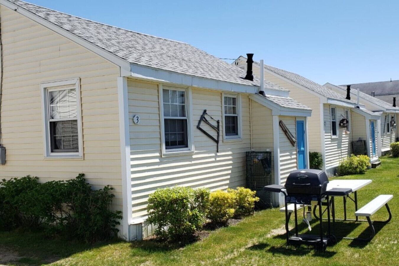 A row of single-story mobile homes with a small patio area, including a grill and picnic table.