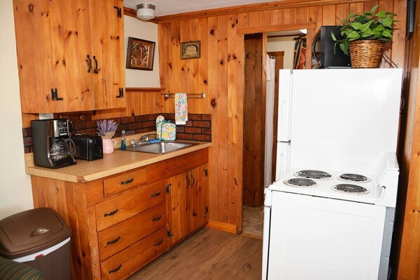 Una cocina compacta con armarios de madera, una estufa blanca, un lavamanos y una cafetera.