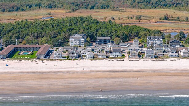Una zona residencial costera con propiedades frente al mar, un hotel con piscina y un bosque denso al fondo.