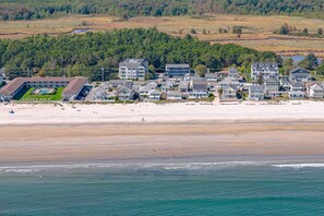 Una zona residencial costera con propiedades frente al mar, un hotel con piscina y un bosque denso al fondo.