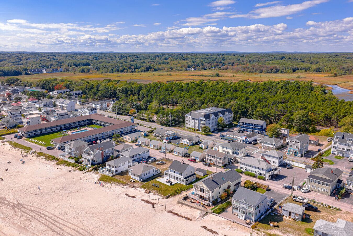 A coastal residential area with beachfront properties, a large building complex, and a forested background.