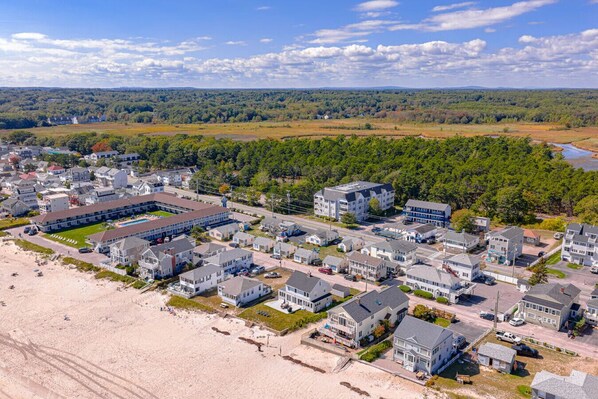 A coastal residential area with beachfront properties, a large building complex, and a forested background.