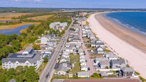 Et kystnært boligområde med huse langs en strand, en vej og en flod i baggrunden.