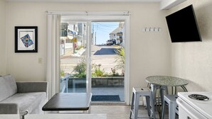 A compact living space with a sofa, a small table, a kitchenette, and a sliding glass door leading to a street view.