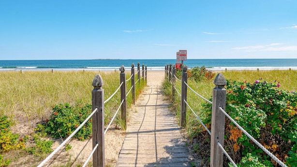 A wooden boardwalk leading to a beach with a clear view of the ocean.