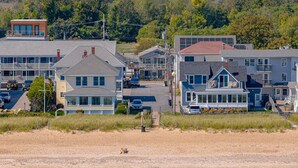 A coastal town with multiple-story buildings, a sandy beach, and a forested hill in the background.