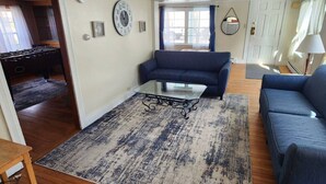 Una sala de estar con un sofá azul, una mesa de centro de vidrio y un tapete estampado.