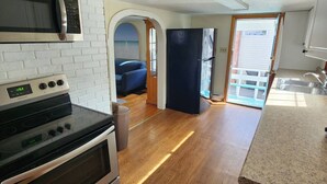 Cocina compacta con microondas, estufa y refrigerador.  Piso de madera y vista al exterior a través de una puerta abierta.