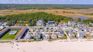 Una zona residencial costera con varias casas de dos pisos, un edificio grande con piscina y una playa en primer plano.