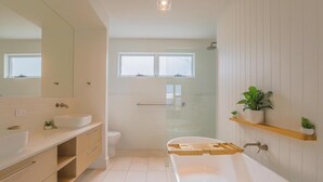 A modern bathroom with a freestanding bathtub, a large mirror, a toilet, and a window. - Cedar Sands Hideaway - 3BRM Home (Gold Coast)