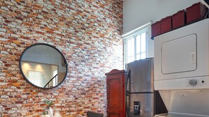 Une cuisine avec un mur en briques, une table en bois avec des chaises, un réfrigérateur et un lave-linge.