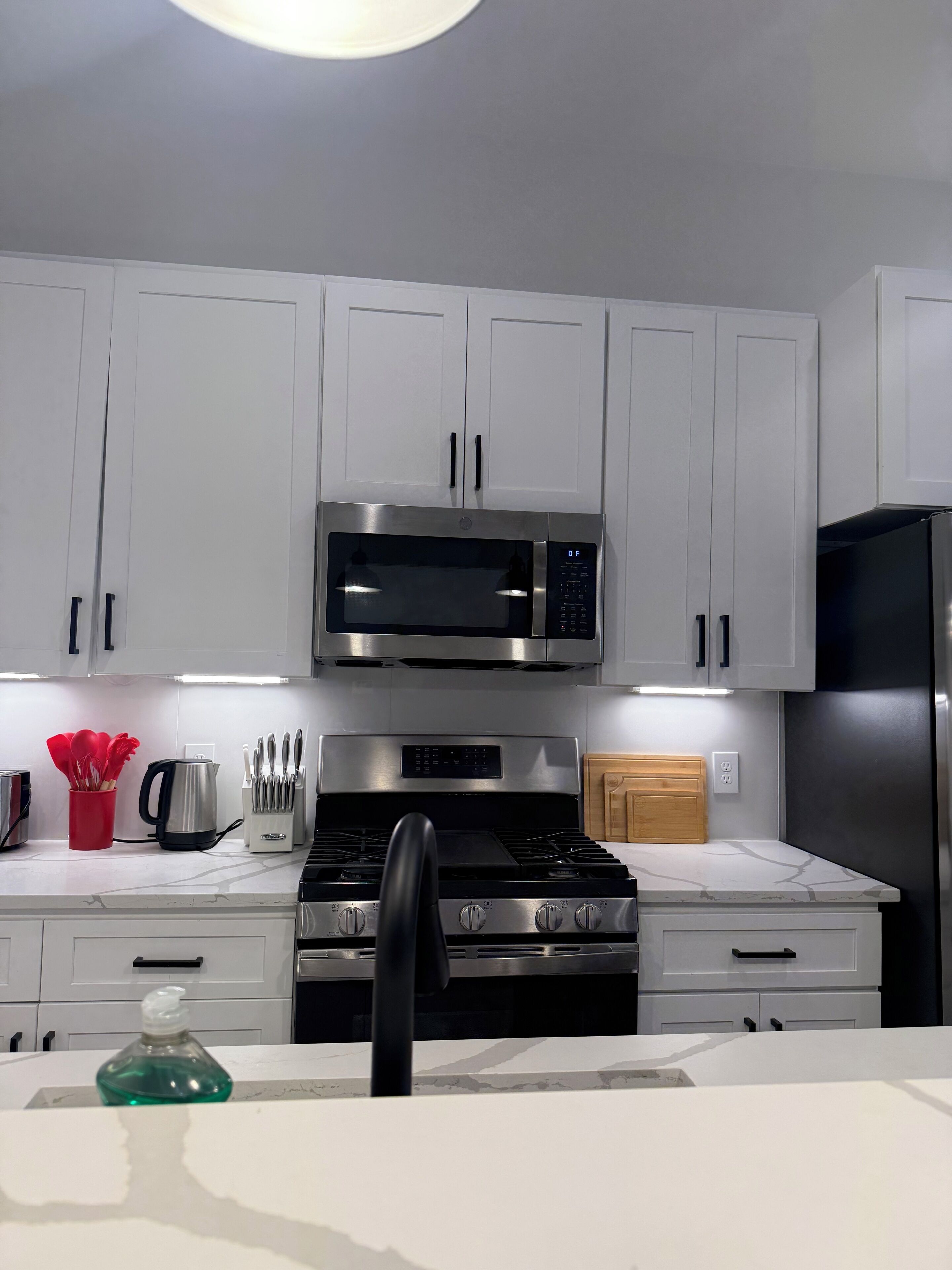 A modern kitchen with white cabinets, a stainless steel microwave, a gas stove, and a black refrigerator.