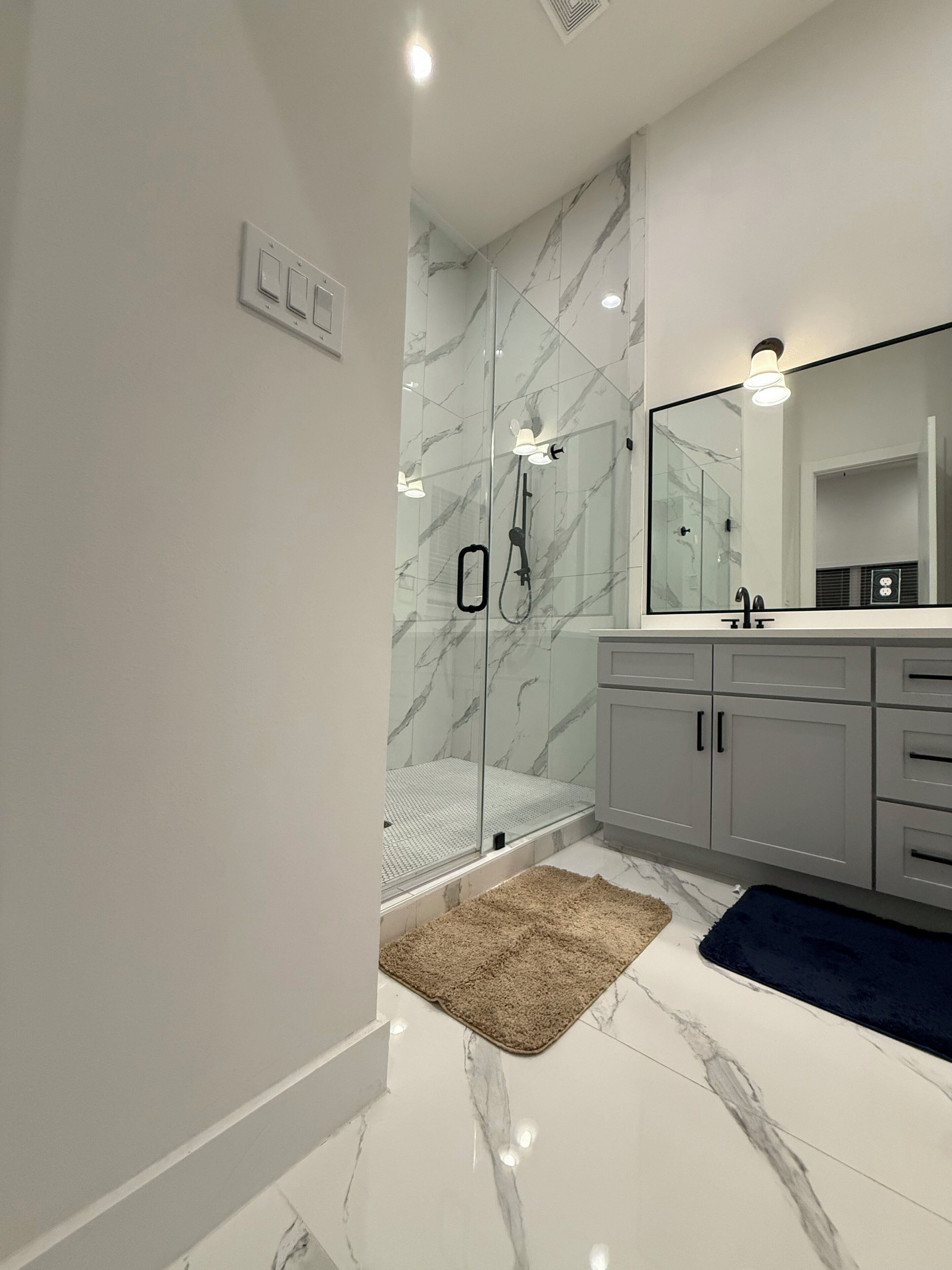 A modern bathroom with a glass shower enclosure, a large mirror, and a marble-tiled floor.