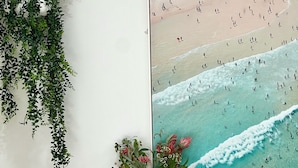 Una parete con una stampa incorniciata raffigurante una spiaggia, una pianta pensile, un vaso con fiori e una pila di libri su un mobile in legno.