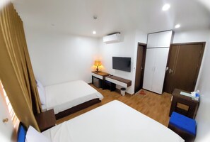 Ein Hotelzimmer mit zwei Betten, einem Schreibtisch mit Lampe, einem Fernseher und einem Kleiderschrank.