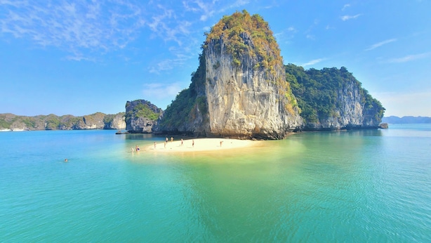 A beach with clear turquoise water and a large limestone rock formation. - Cat Ba Charm Island Hotel (Hai Phong)