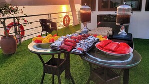 A table with food and drinks, a chair, and a view of the water and mountains. - Cat Ba Charm Island Hotel (Hai Phong)