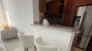 Una cocina moderna con una isla central, dos taburetes blancos tipo bar, armarios de madera y electrodomésticos de acero inoxidable.