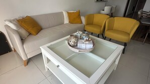 Una sala de estar con un sofá blanco, sillones amarillos y una mesa de centro de vidrio con adornos.
